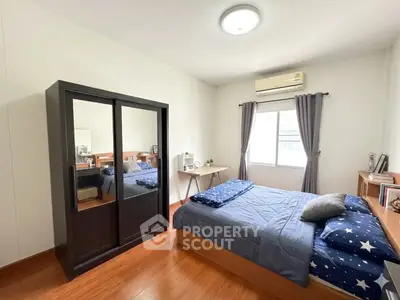 Cozy bedroom with wooden flooring, stylish wardrobe, and natural light from window.