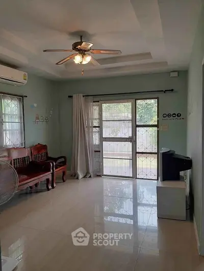 Spacious living room with ceiling fan and natural light, featuring classic wooden furniture and a large window.