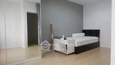 Modern minimalist bedroom with mirrored wardrobe and sleek wooden flooring.