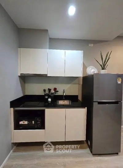 Modern kitchen with sleek cabinets, black countertop, and stainless steel fridge in a stylish apartment.