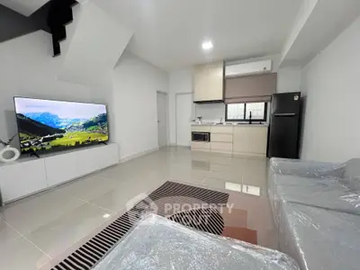 Modern open-plan living room with sleek kitchen, large TV, and stylish furniture in a contemporary apartment.