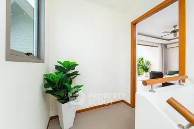 Bright hallway leading to a modern living room with large windows and lush greenery view.