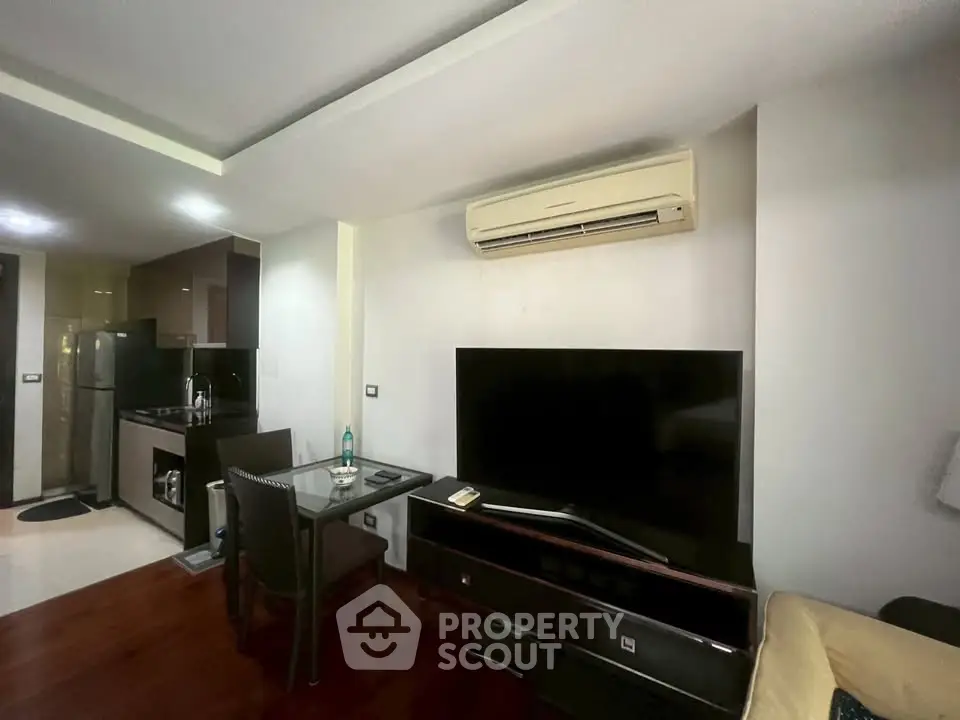 Modern living room with sleek kitchen, featuring air conditioning and large TV for comfortable urban living.