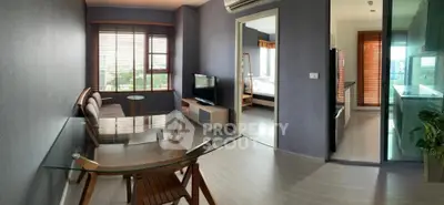 Modern apartment interior with glass dining table, cozy living area, and view into bedroom and kitchen.