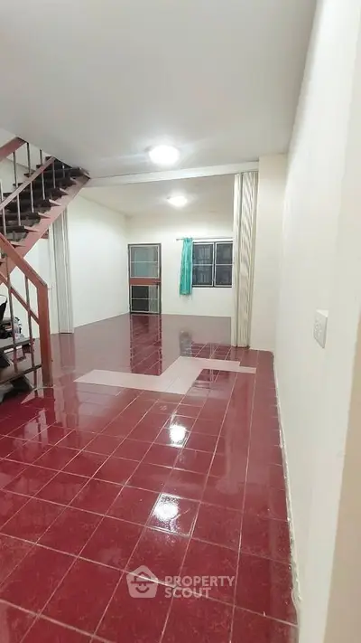 Spacious living room with glossy red tile flooring and staircase, ideal for modern living.
