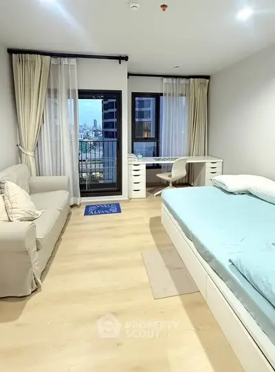 Modern bedroom with city view, featuring a cozy bed, stylish sofa, and a functional desk by the window.