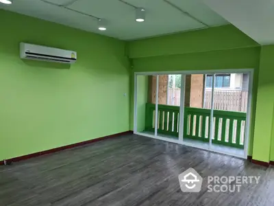 Vibrant green-walled spacious room with modern air conditioning unit and large windows leading to a cozy balcony, perfect for entertaining.