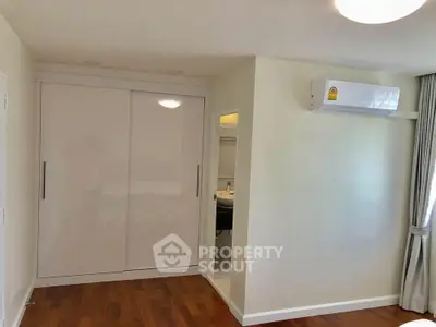 Modern bedroom with wooden flooring, built-in wardrobe, and air conditioning unit.