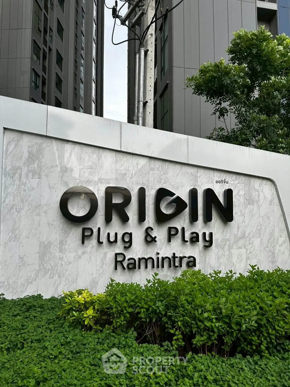 Modern building exterior with Origin Plug & Play Ramintra signage surrounded by lush greenery.