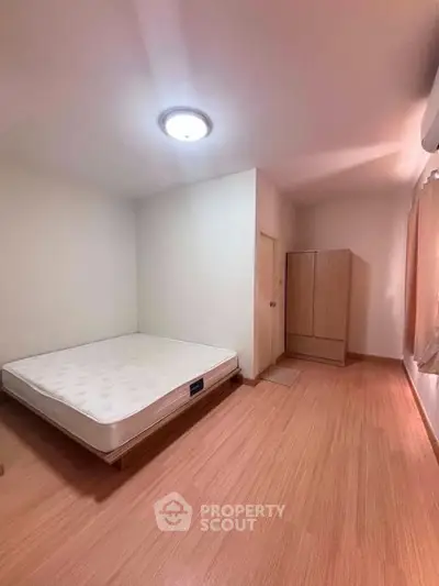 Spacious bedroom with minimalist design and wooden flooring, featuring a comfortable bed and wardrobe.