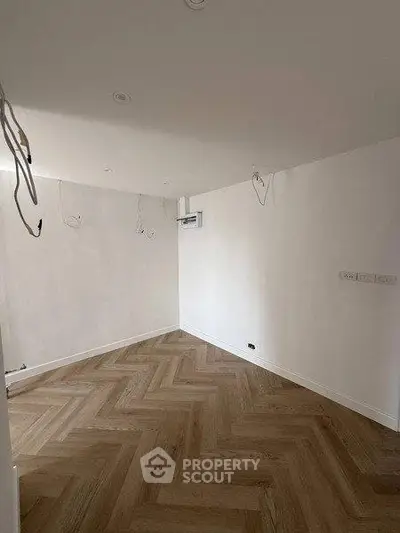 Spacious unfurnished room with elegant herringbone wood flooring and white walls, ideal for customization.