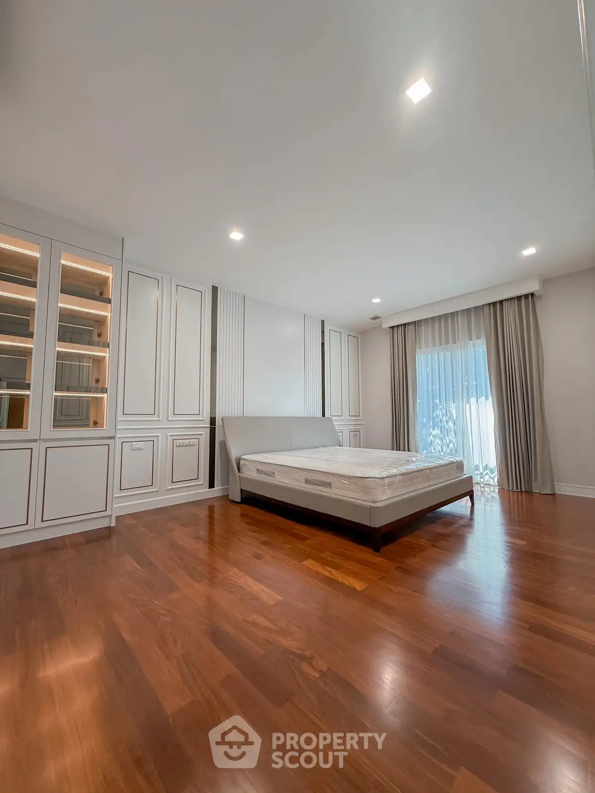 Spacious bedroom with elegant wooden flooring and large window for natural light.