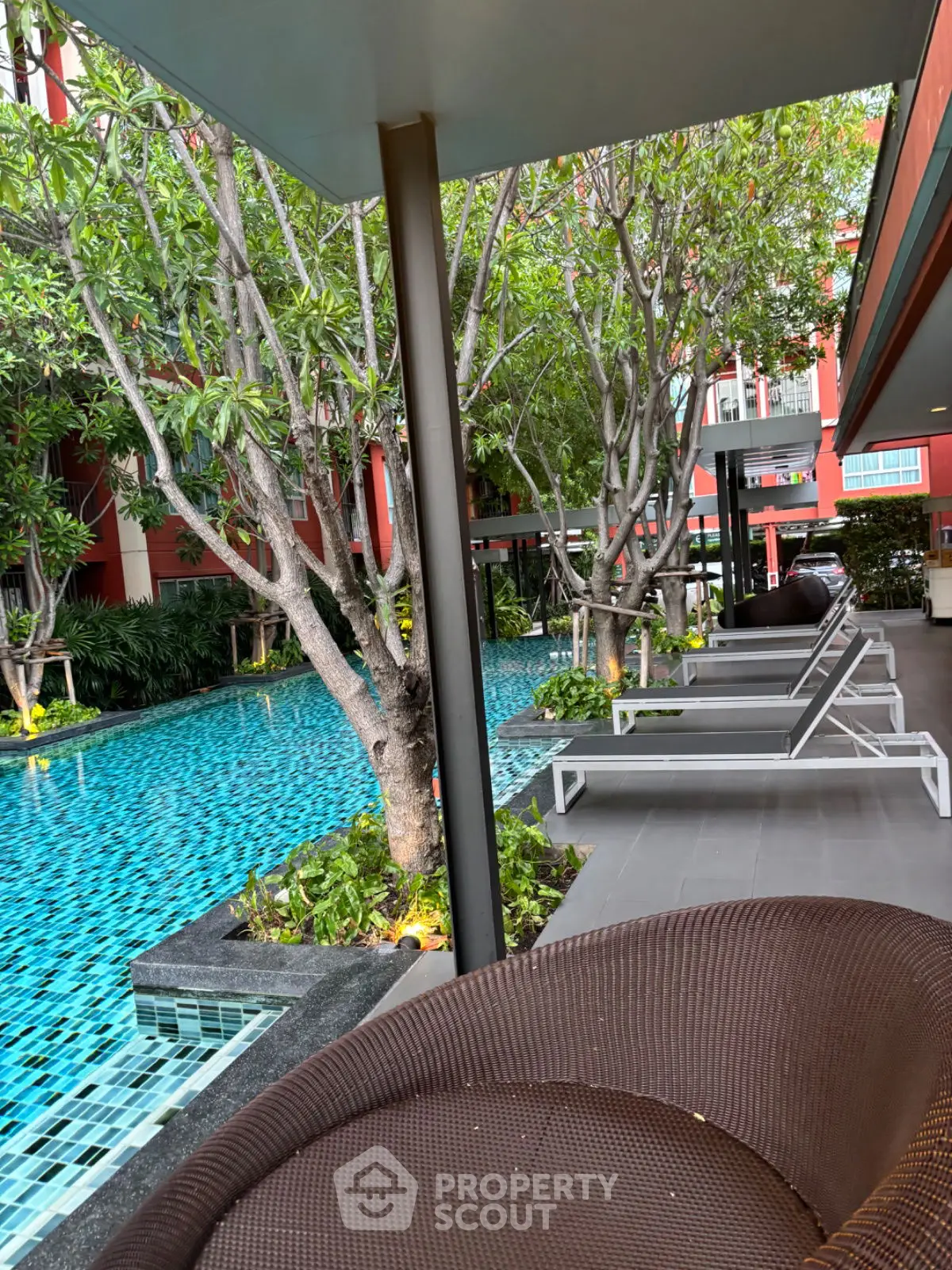 Luxurious poolside area with modern lounge chairs and lush greenery in a stylish residential complex.
