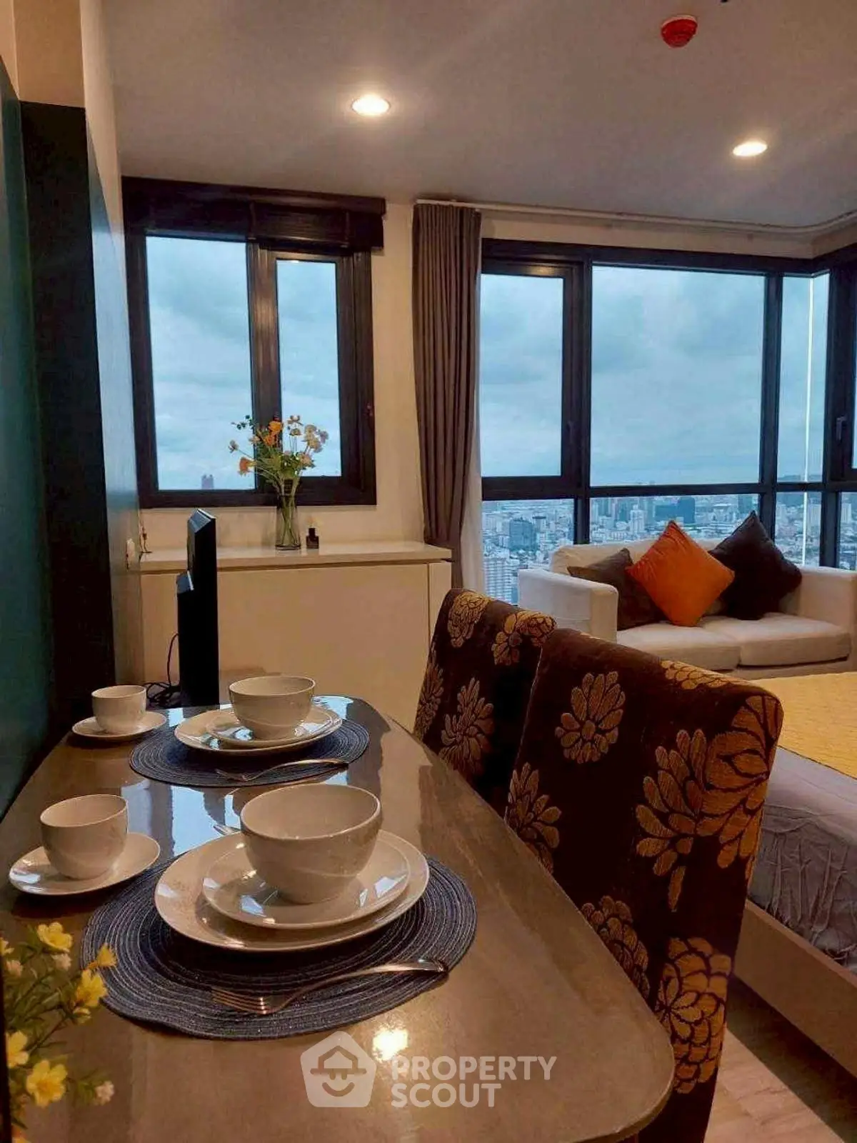 Modern living room with city view, stylish decor, and dining area in high-rise apartment.