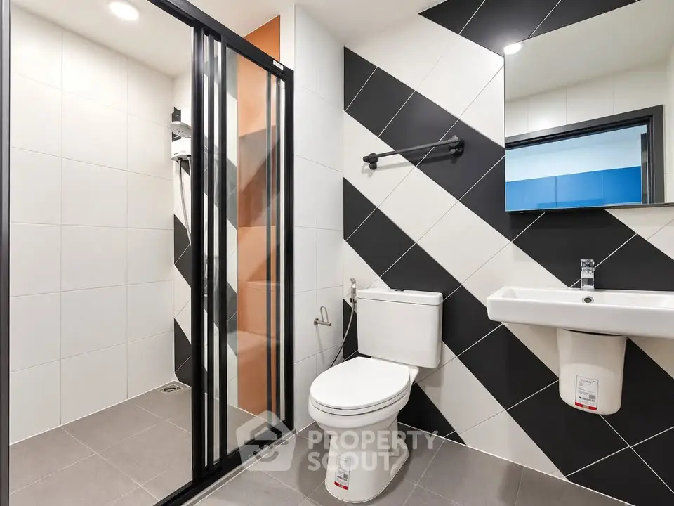Modern bathroom with sleek black and white tile design and glass shower enclosure.