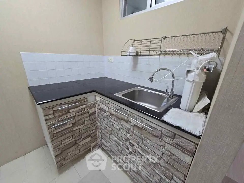 Modern kitchen with sleek black countertop and stone-patterned cabinets, featuring a stainless steel sink and water filter.