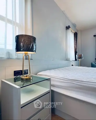 Modern bedroom with stylish lamps and natural light, featuring a cozy bed and elegant decor.