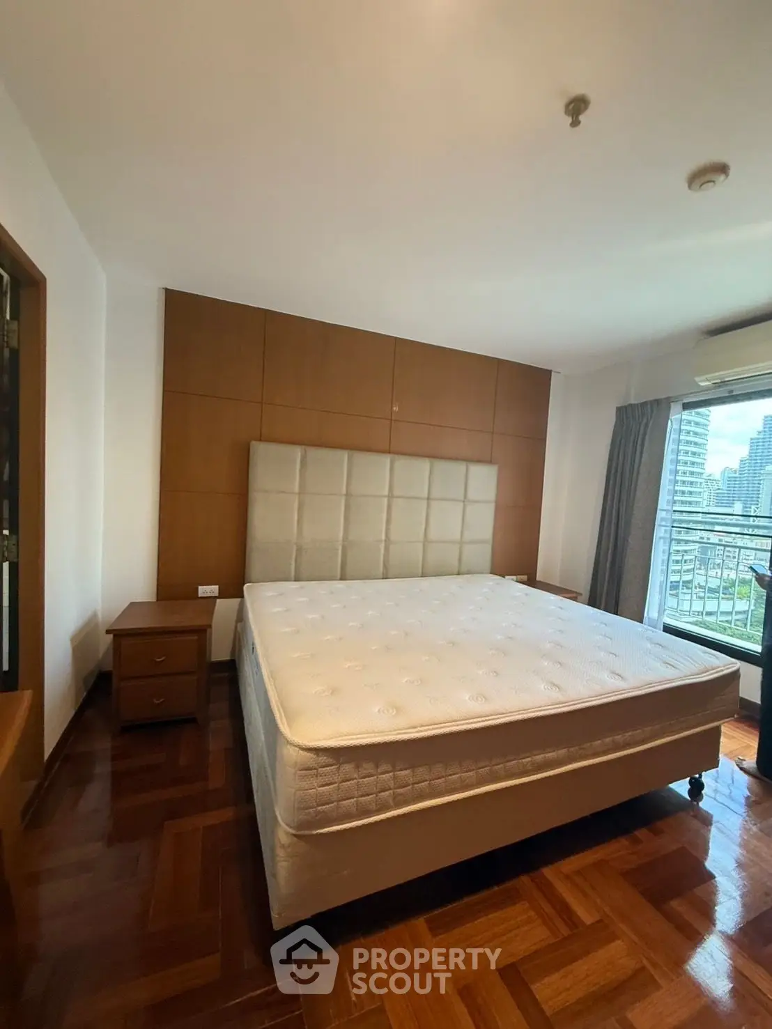 Spacious bedroom with large bed and city view, featuring elegant wooden flooring and modern design.