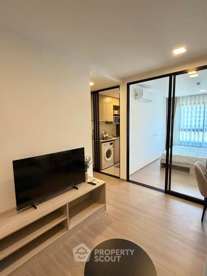 Modern apartment interior with living room, kitchen, and bedroom view, featuring sleek design and natural lighting.