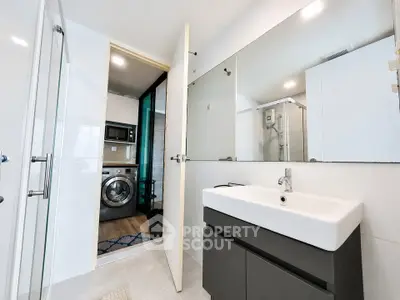 Modern bathroom with sleek sink and washing machine in adjacent laundry area.