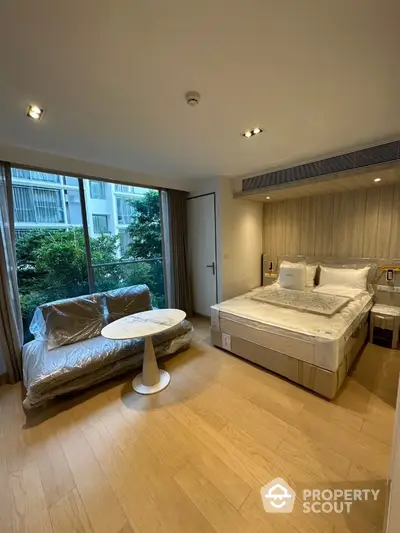 Modern bedroom with large window and cozy seating area in a stylish apartment.