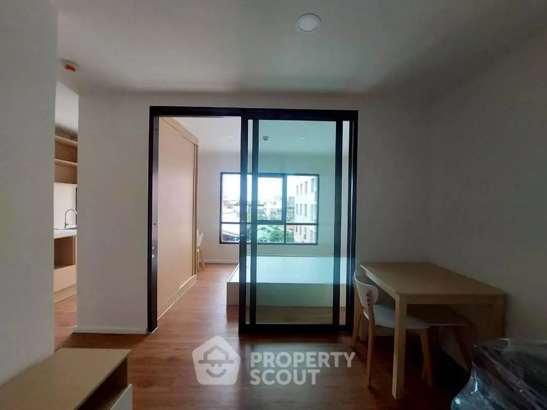 Modern apartment interior with glass partition, wooden flooring, and compact dining area.