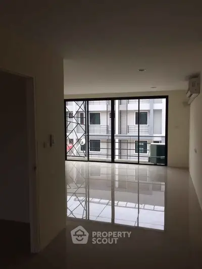 Spacious modern living room with large windows and glossy tiled floors in a contemporary apartment.