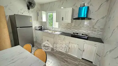 Modern kitchen with marble countertops, gas stove, and stainless steel fridge in a bright, airy space.
