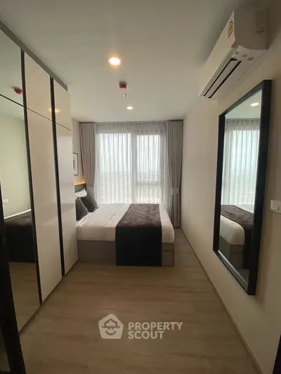 Modern bedroom with large window, mirrored wardrobe, and air conditioning in a stylish apartment.
