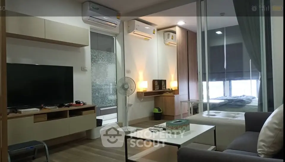 Modern living room with sleek furniture and glass partition leading to a cozy bedroom.