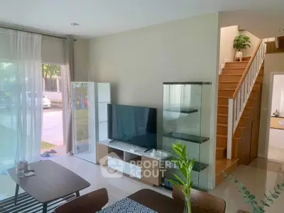 Modern living room with sleek TV setup and glass cabinets, adjacent to a stylish wooden staircase.