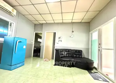 Spacious living room with modern black sofa and vibrant blue fridge, featuring tiled flooring and ample natural light.