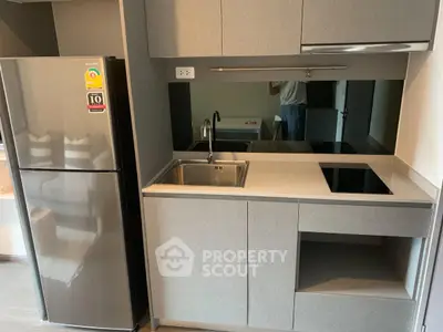 Modern compact kitchen with sleek cabinetry and stainless steel fridge in a stylish apartment.