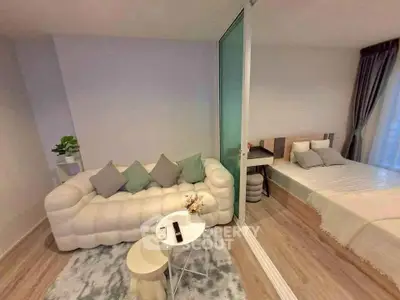 Modern living room with cozy sofa and adjacent bedroom in open layout apartment.