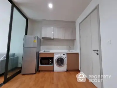 Modern compact kitchen with washing machine and stainless steel fridge in cozy apartment.