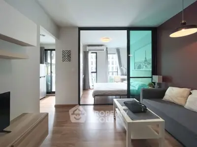 Modern open-plan living room with glass partition leading to a cozy bedroom, featuring stylish decor and natural light.