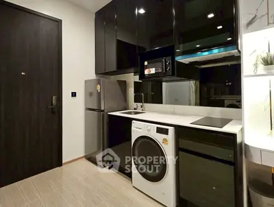 Modern kitchen with sleek black cabinets, fridge, washing machine, and induction cooktop.