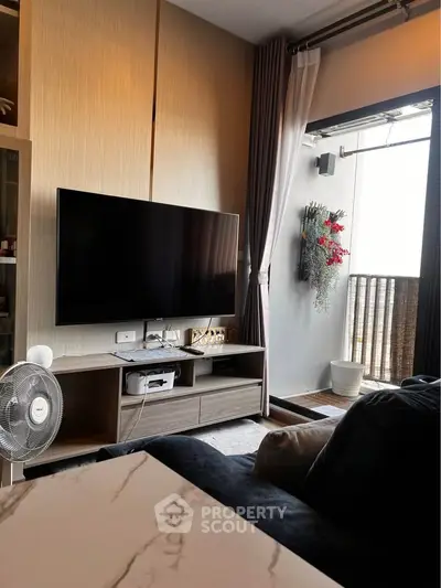 Modern living room with large TV and balcony access, featuring stylish decor and natural light.
