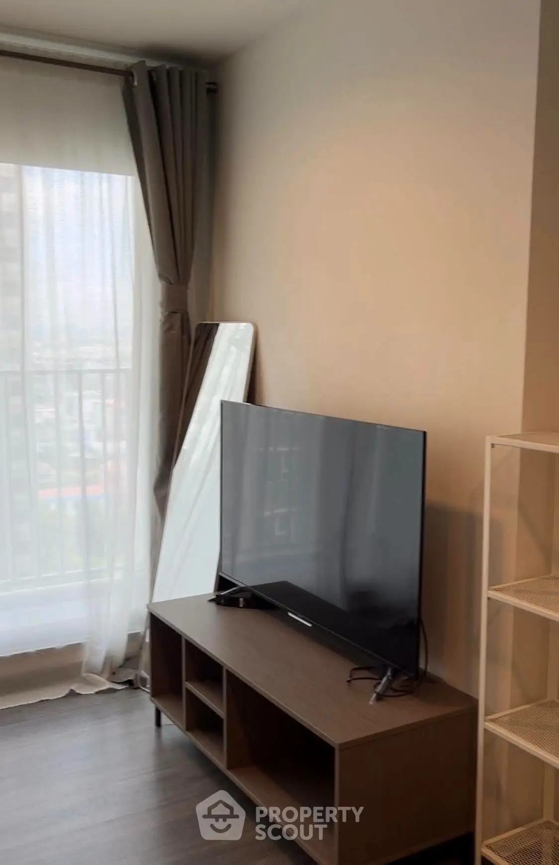 Modern living room with large TV and floor-to-ceiling window offering city views.