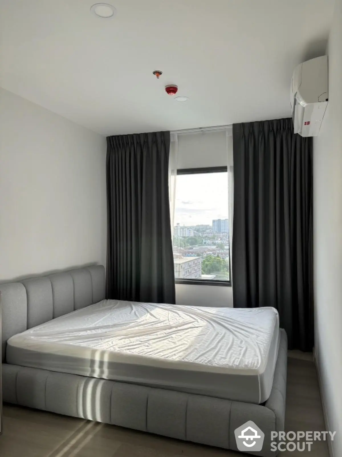 Modern bedroom with large window and city view, featuring a stylish bed and air conditioning.