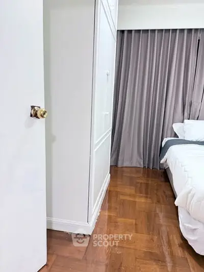 Cozy bedroom with elegant wooden flooring and soft curtains, featuring a comfortable bed and ample closet space.