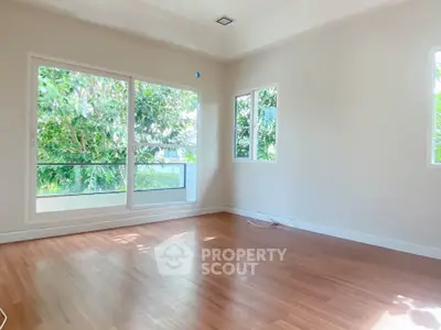 Bright empty room with large windows and wooden flooring, offering a serene view of lush greenery.