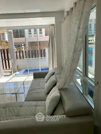Bright living room with modern sofa and glass table overlooking a private pool.