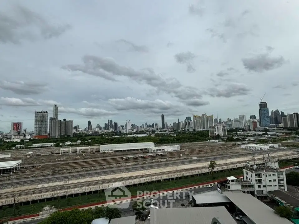 Panoramic cityscape view showcasing urban skyline and railway tracks under a cloudy sky.