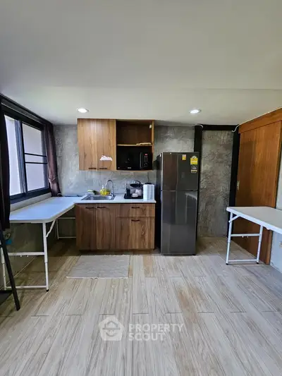 Modern kitchen with stainless steel fridge and wooden cabinets in a bright, spacious layout.
