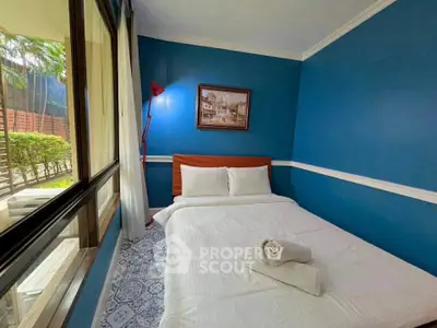 Cozy bedroom with blue walls and large window overlooking garden, featuring a comfortable bed and elegant decor.