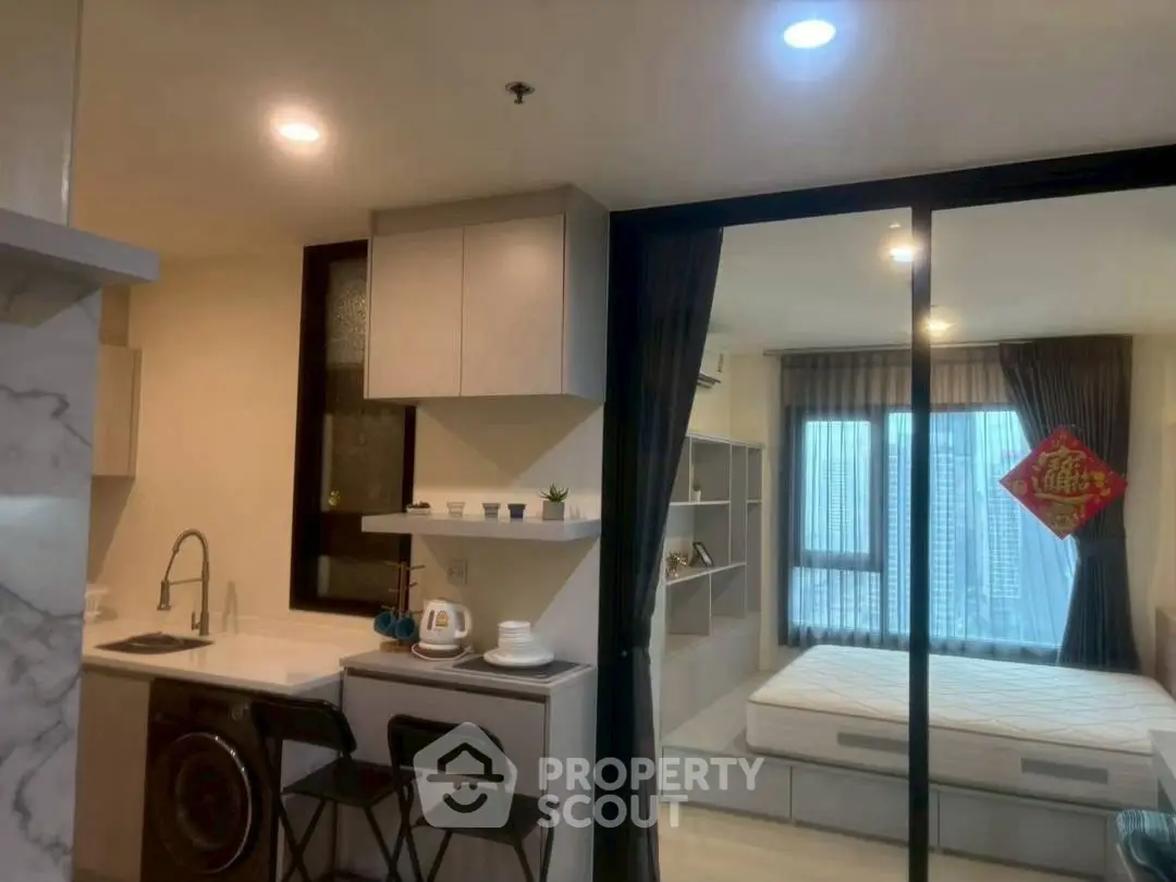 Modern studio apartment with compact kitchen and cozy sleeping area, featuring city views.