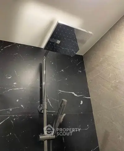 Modern bathroom shower with sleek black marble tiles and square rain showerhead.
