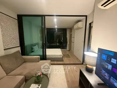 Modern studio apartment with open layout, featuring a cozy living area and bedroom separated by glass partition.