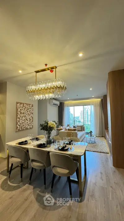 Luxurious open-plan living and dining area with elegant chandelier and city view.